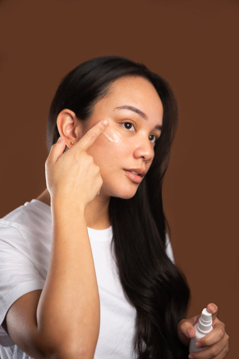 Woman applying curative serum to her face against a brown background