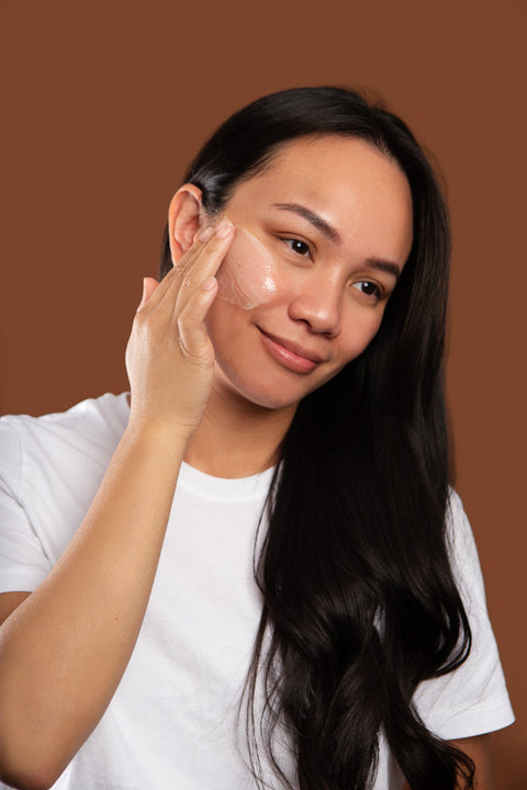 Woman applying marigold cleansing balm to her face against a brown background