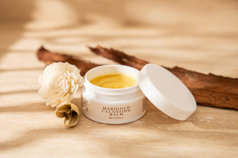 Jar of Marigold Calming Balm with a white flower on a beige fabric background