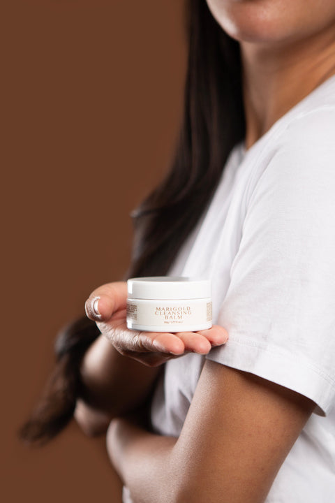 model holding marigold cleansing balm in palm against brown background