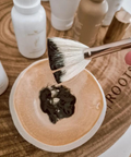 Makeup brush with black and white powder on a wooden surface with skincare products.