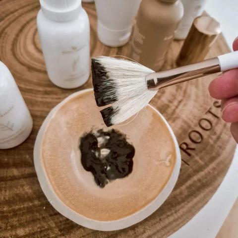 Makeup brush with black and white powder on a wooden surface with skincare products.