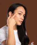 Woman applying curative serum to her face against a brown background