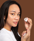 Woman holding a small white container against a brown background