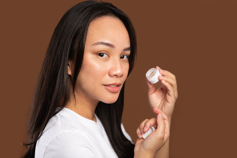 Woman holding a small white container against a brown background