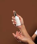 Hand holding a white spray bottle with a brown background
