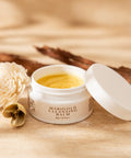 Jar of Marigold Calming Balm with a white flower on a beige fabric background