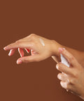Hand applying curative serum to another hand against a brown background