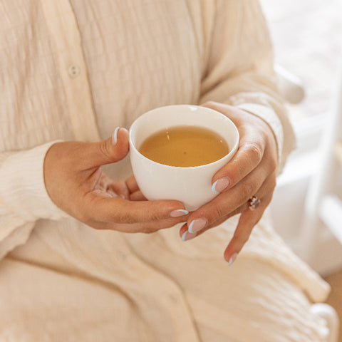 Woman holding a cup of Bare Roots Wholesome Beauty Tea, enjoying a calming tea moment.