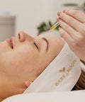 Omega Oil being gently applied to a woman's face during a facial, illustrating its nourishing, professional use.