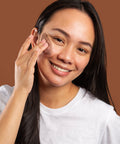 Woman applying makeup on her face against a brown background