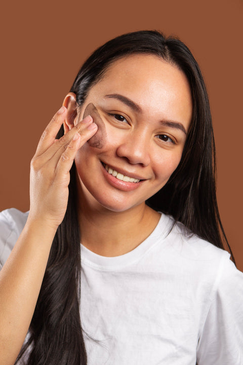Woman applying makeup on her face against a brown background