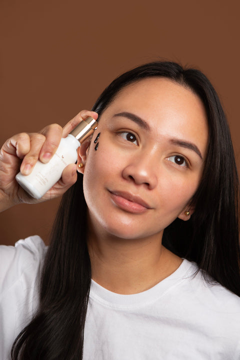 Woman applying skincare product to her face against a brown background