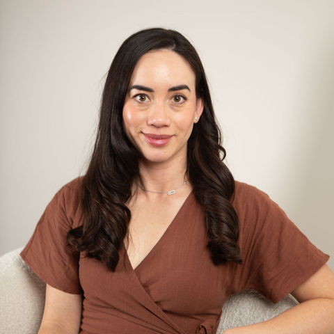 Woman in a brown dress sitting on a light-colored couch against a plain background