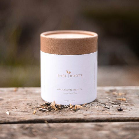 Bare Roots Wholesome Beauty Tea pouch on a wooden surface with loose tea leaves sprinkled around.