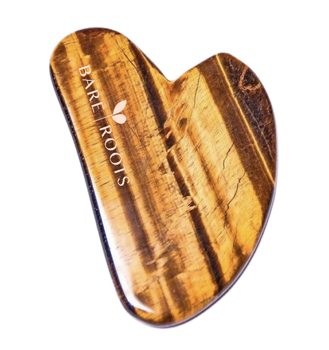 A heart-shaped Gua sha massage tool made of polished tiger's eye stone, featuring natural golden-brown and black stripes. The brand name 'BARE ROOTS' is printed in white on the upper left side.