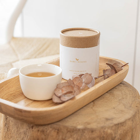 Bare Roots Wholesome Beauty Tea displayed on a wooden stand beside a steaming cup of tea.