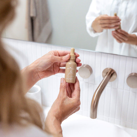 Woman holding Clarity Serum bottle near a sink in a bathroom setting