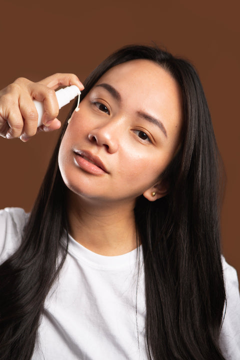 woman applying curative serum to cheek against brown backdrop