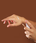 Hand applying curative serum to another hand against a brown background