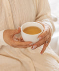 Woman holding a cup of Bare Roots Wholesome Beauty Tea, enjoying a calming tea moment.