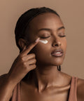 Woman applying cream to her face against a beige background