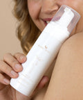 Woman holding Bare Roots Gentle Foaming Cleanser bottle, smiling.