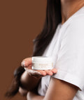 model holding marigold cleansing balm in palm against brown background