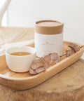 Bare Roots Wholesome Beauty Tea displayed on a wooden stand beside a steaming cup of tea.