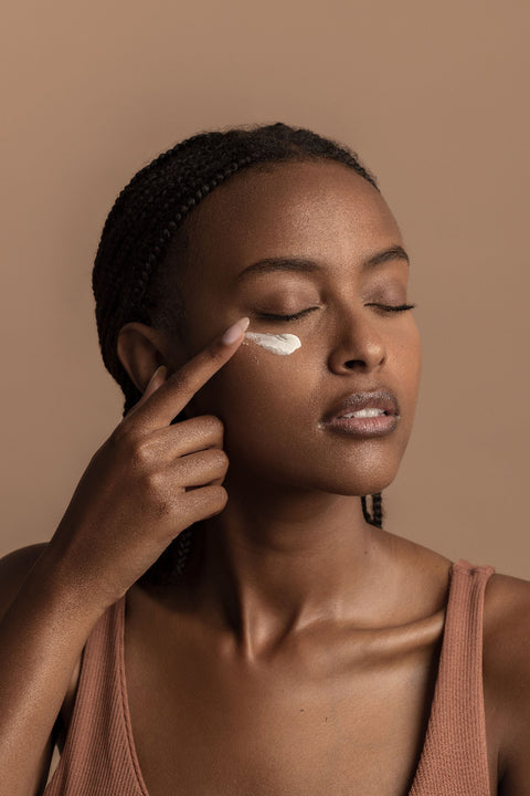 Woman applying cream to her face against a beige background
