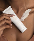 Person holding a tube of skincare product on their skin with a visible application mark.