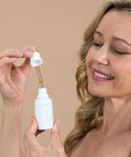 A woman gently holding a dropper of Bare Roots Omega Oil, ready to apply it to her skin.