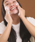 model smiling as she massages gentle foaming cleanser into skin
