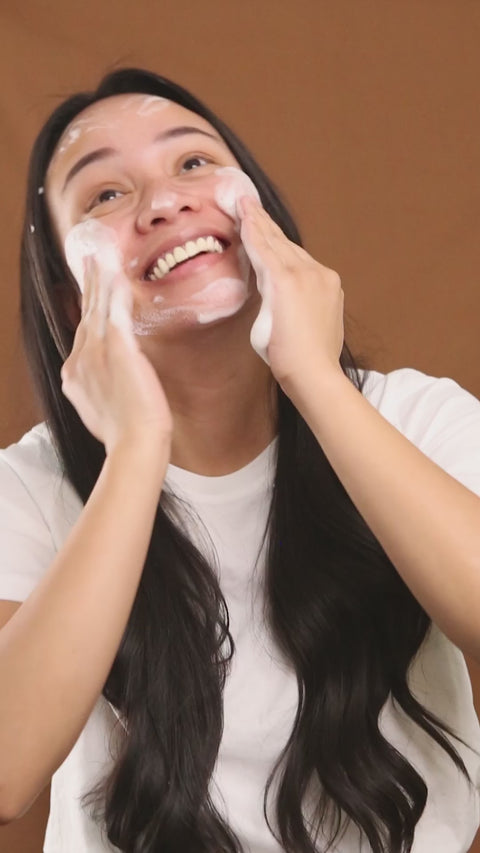 model smiling as she massages gentle foaming cleanser into skin